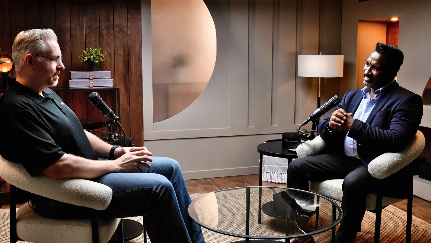 Dave Upton and Suresh Devanan in conversation across a low table in the OUTCOME / AI studio, each at a microphone